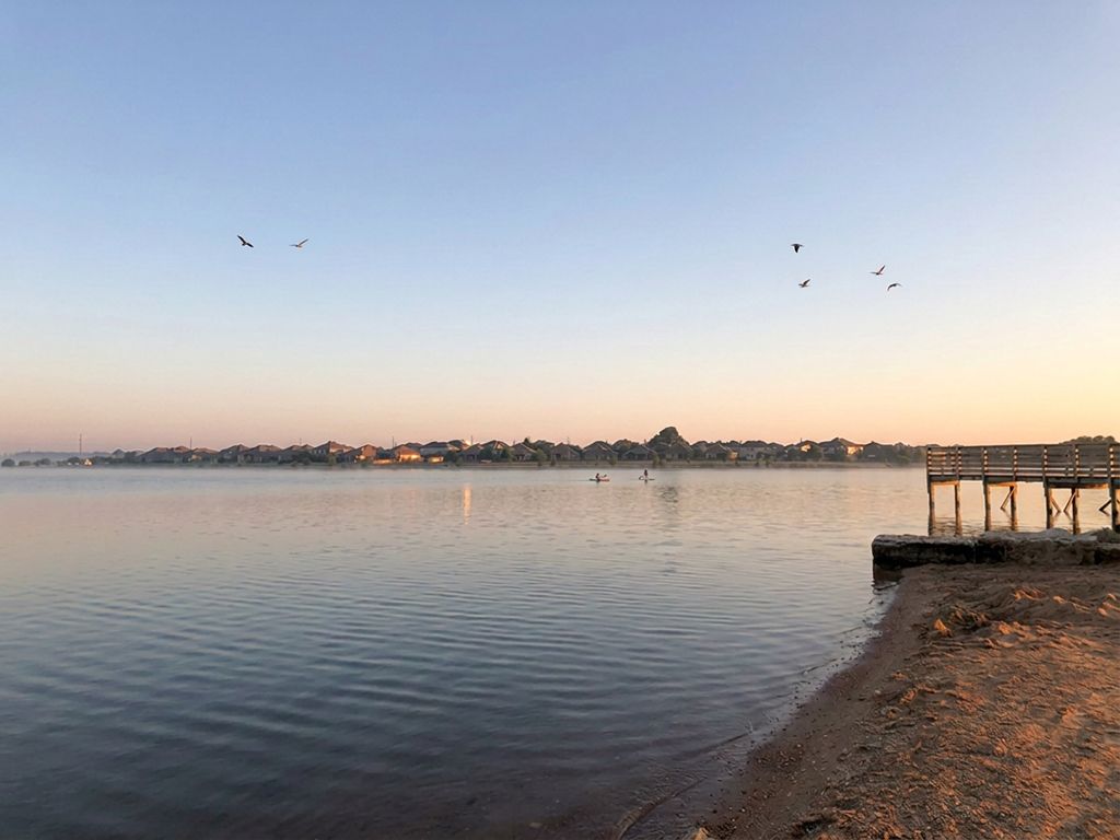 Lake Pflugerville at sunset with calm water, native grasses, and a paved shoreline trail